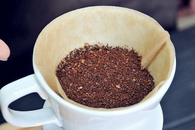 A ceramic pour-over dripper with a paper filter seated inside and ground coffee added